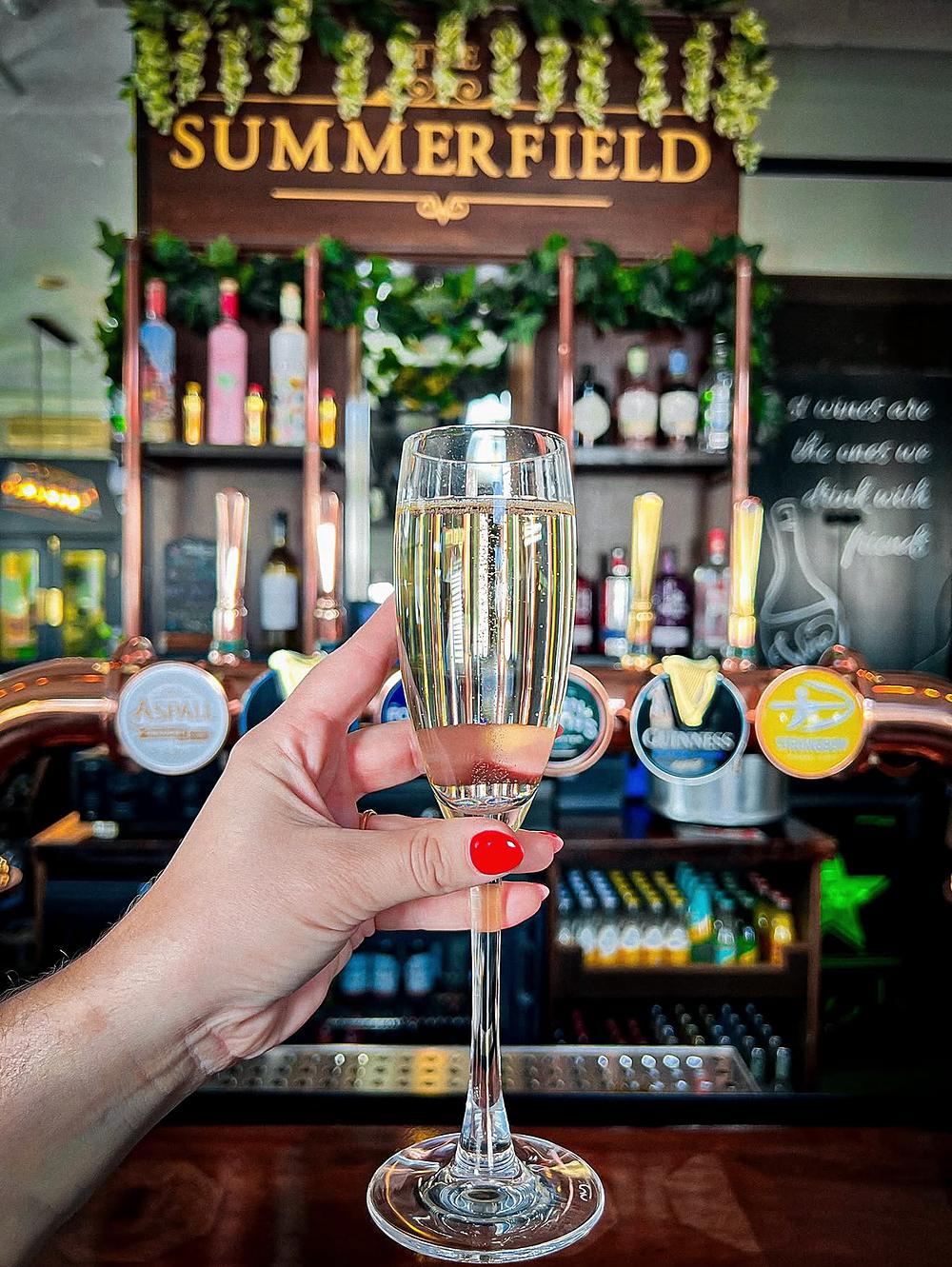A glass of fizz raised at the bar under the Summerfield sign