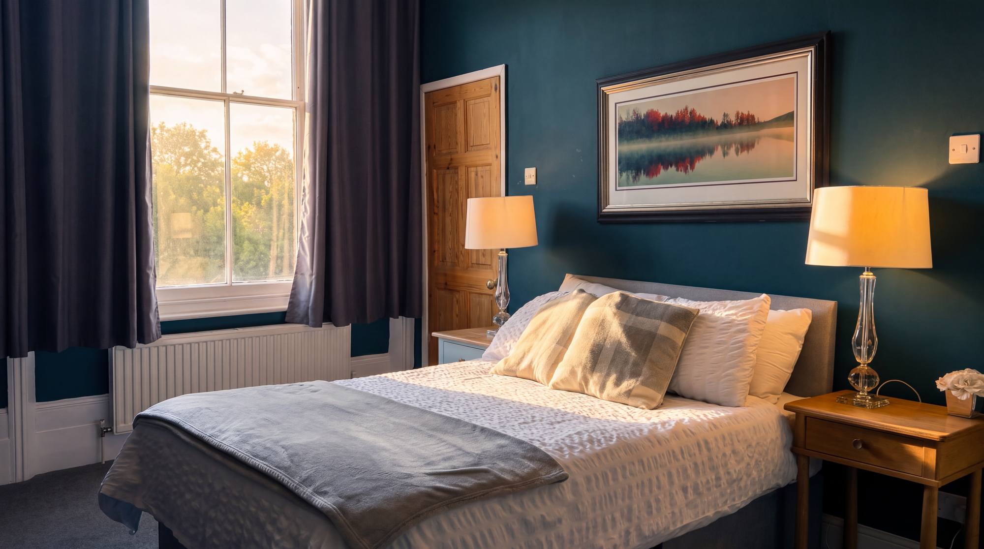 A guest room - a double bed with grey throw, brass lamps and teal walls
